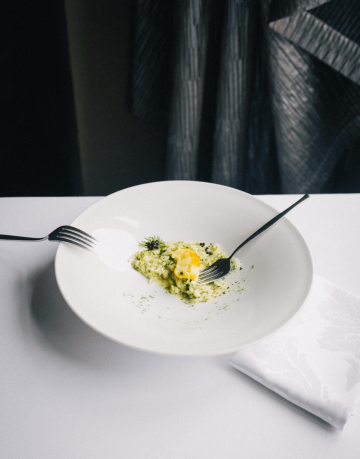 Rozjedené elegantně servírované risotto s bylinkami a vaječným žloutkem na bílém talíři ve fine dining restauraci Bellevue.