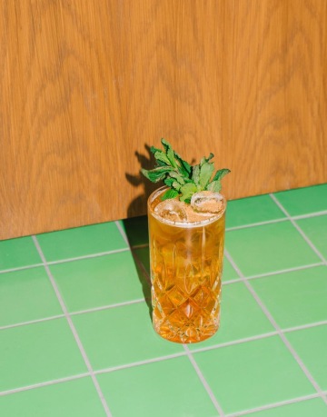 Osvěžující koktejl s mátou a ledem ve vysoké sklenici na zelené dlažbě v baru Kino Přítomnost.