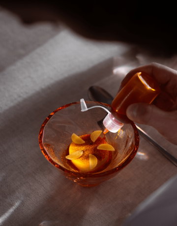 Kuchař Petr Bartoš z Kruh Dining zdobí chod z dýně v oranžové skleněné misce kapkami omáčky pomocí malé lahvičky.