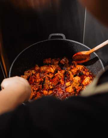 Kuchařka míchá pikantní kousky masa v hrnci v kuchyni restaurace La Bu La.